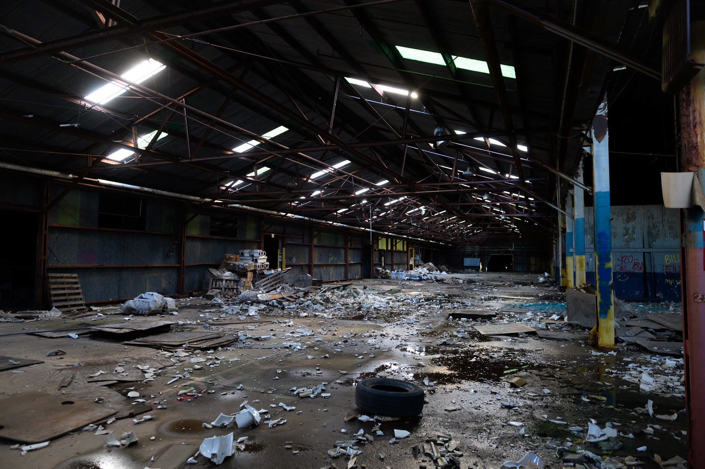 The vast interior of an abandoned factory with broken ceramic pieces littering the wet concrete — abandoned places photography in East Texas by Kaden Baker