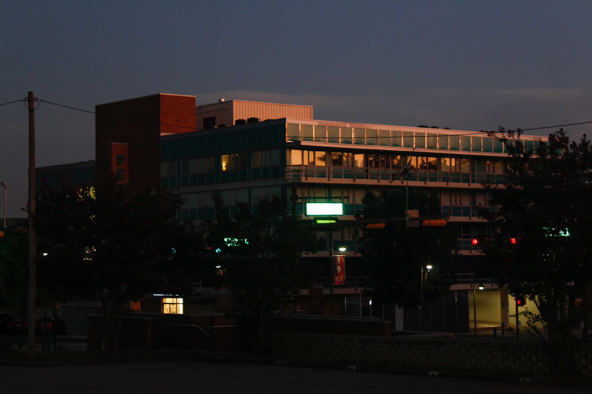 A mid-century modern office building at dusk with golden sunlight reflecting on its upper glass windows above — city photography in East Texas by Kaden Baker